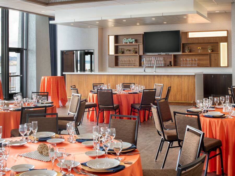 Restaurante com várias mesas preparadas para refeições, área de bar e uma grande televisão na parede.