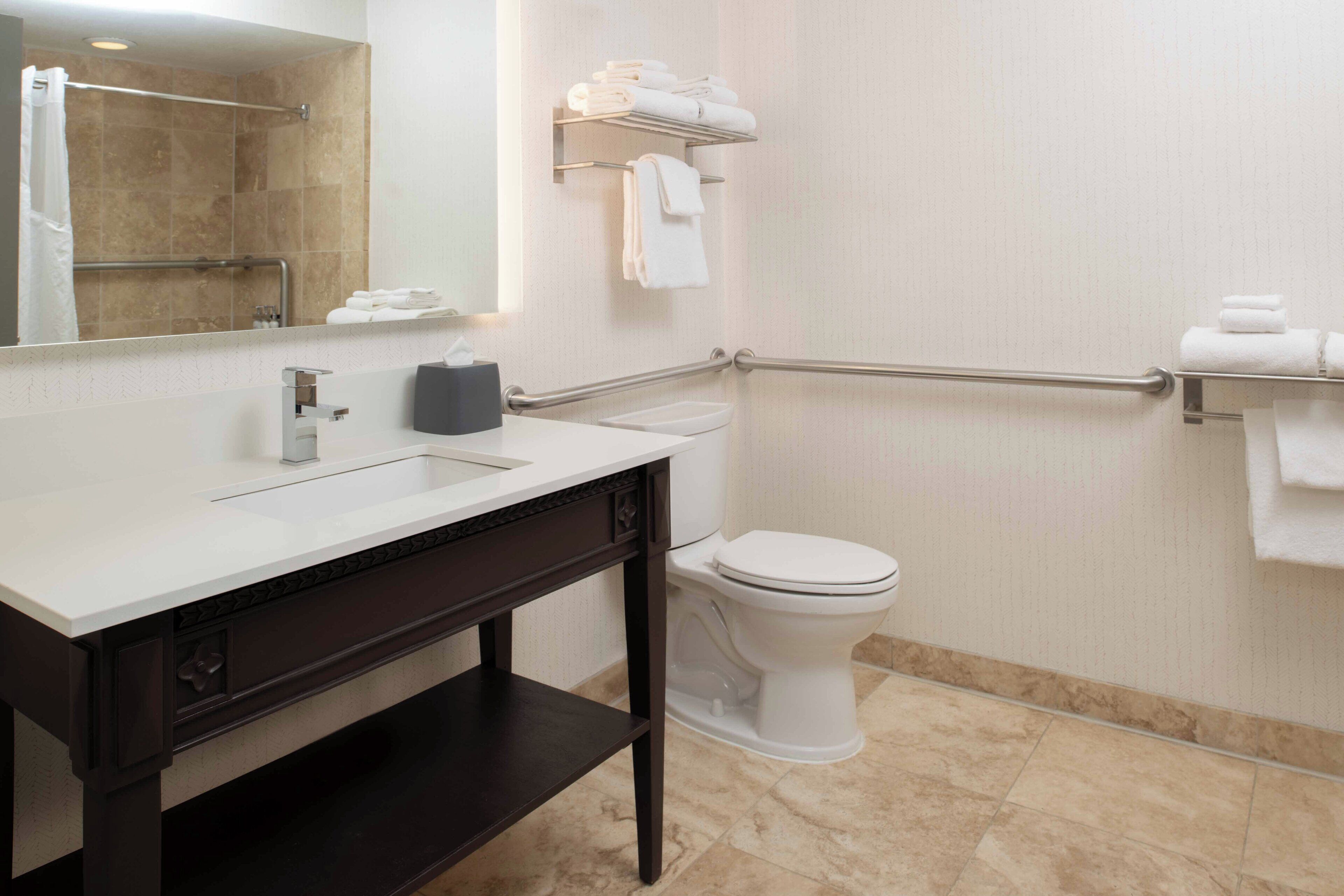 Un baño moderno con un lavamanos blanco, tocador de madera oscura, un inodoro y un perchero para toallas.