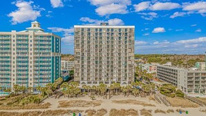 A beachfront hotel with multiple floors, balconies, and a beach area with palm trees. - Sun N Sand Resort (Myrtle Beach)