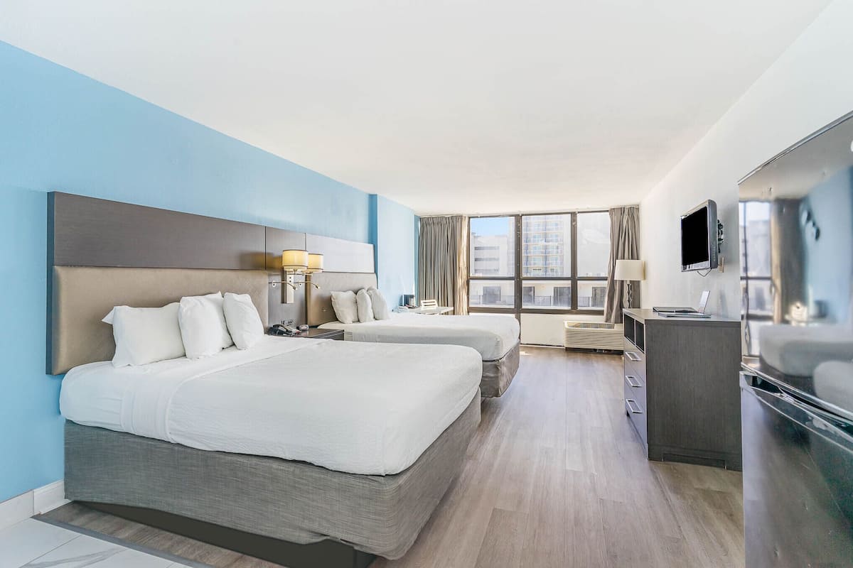 A hotel room with two beds, a desk, and a TV.