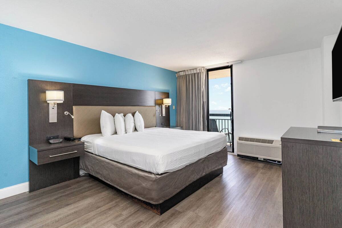 A hotel room with a large bed, bedside lamps, a desk, and a view of the outdoors.