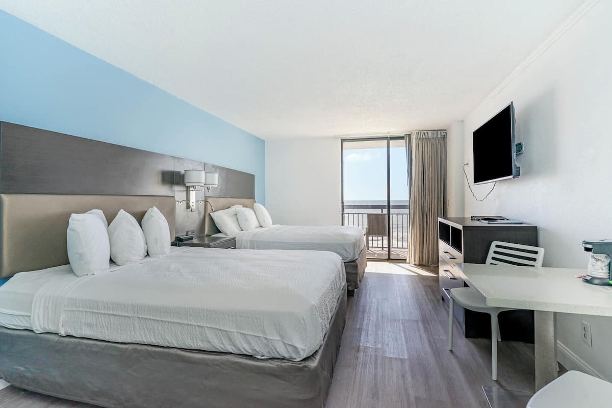 A hotel room with two beds, a desk, a TV, and a balcony with a view.
