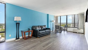 A spacious room with a blue wall, a black leather sofa, a small wooden table, and a chair. - Sun N Sand Resort (Myrtle Beach)