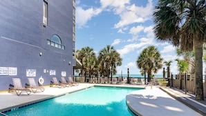 A swimming pool with lounge chairs, palm trees, and a view of the ocean. - Sun N Sand Resort (Myrtle Beach)