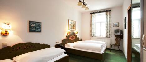 Habitación de hotel con dos camas, alfombra verde, cabecero de madera, lámpara de pared y ventana con cortinas.