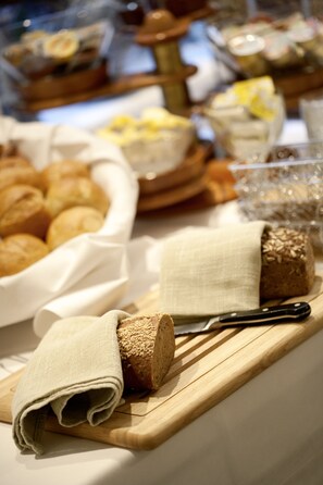 A buffet table with various food items including bread, pastries, and a knife. - Hahn Hotel (Munich)