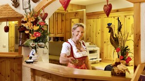 A woman in traditional attire at a wooden counter with floral arrangements and heart-shaped decorations. - Hahn Hotel (Munich)