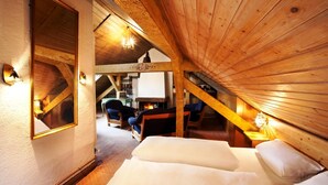 A cozy attic bedroom with a wooden ceiling, a large mirror, and a fireplace. - Hahn Hotel (Munich)