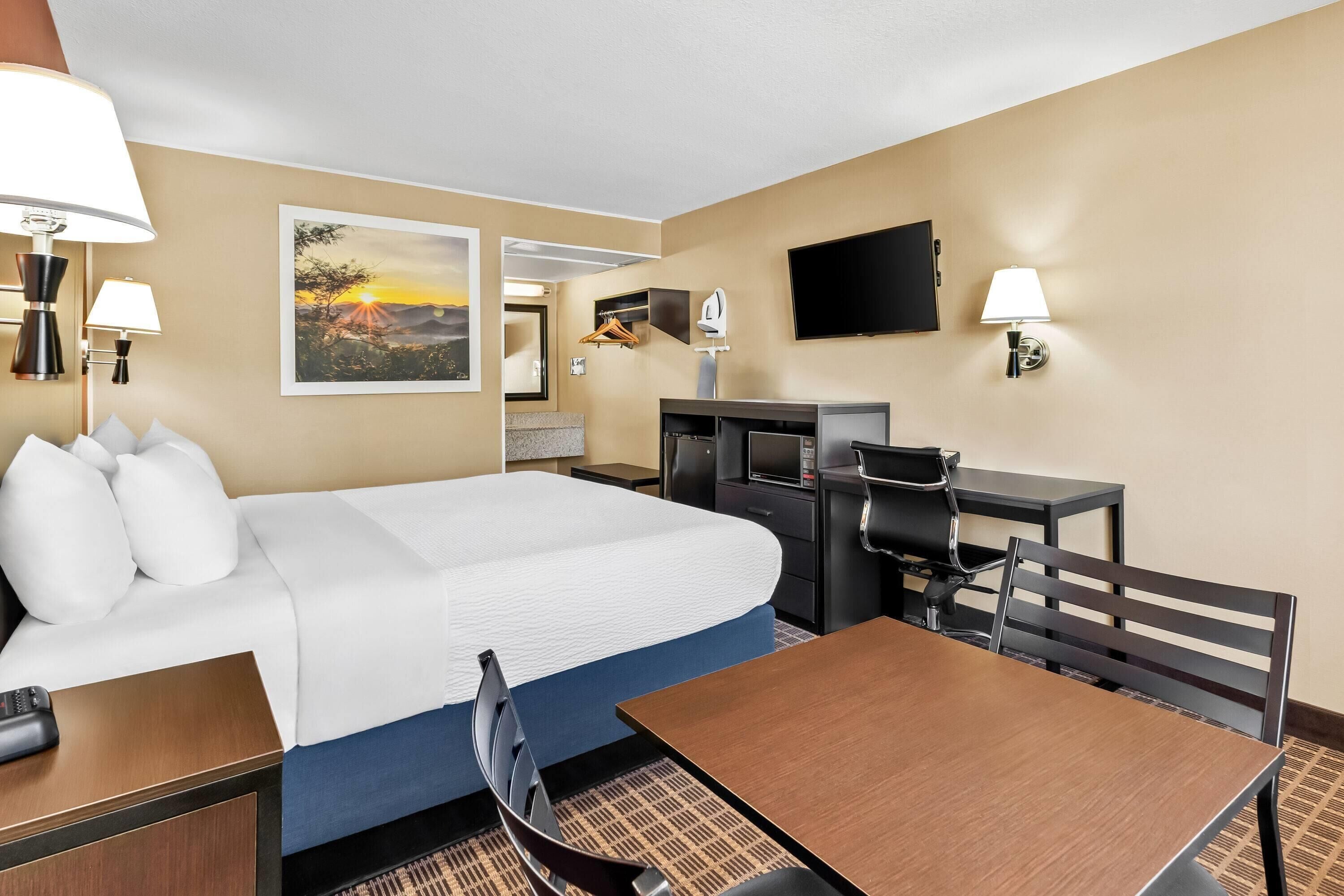 Ein Hotelzimmer mit Bett, Schreibtisch, Stuhl, Fernseher und einem Kunstwerk an der Wand.
