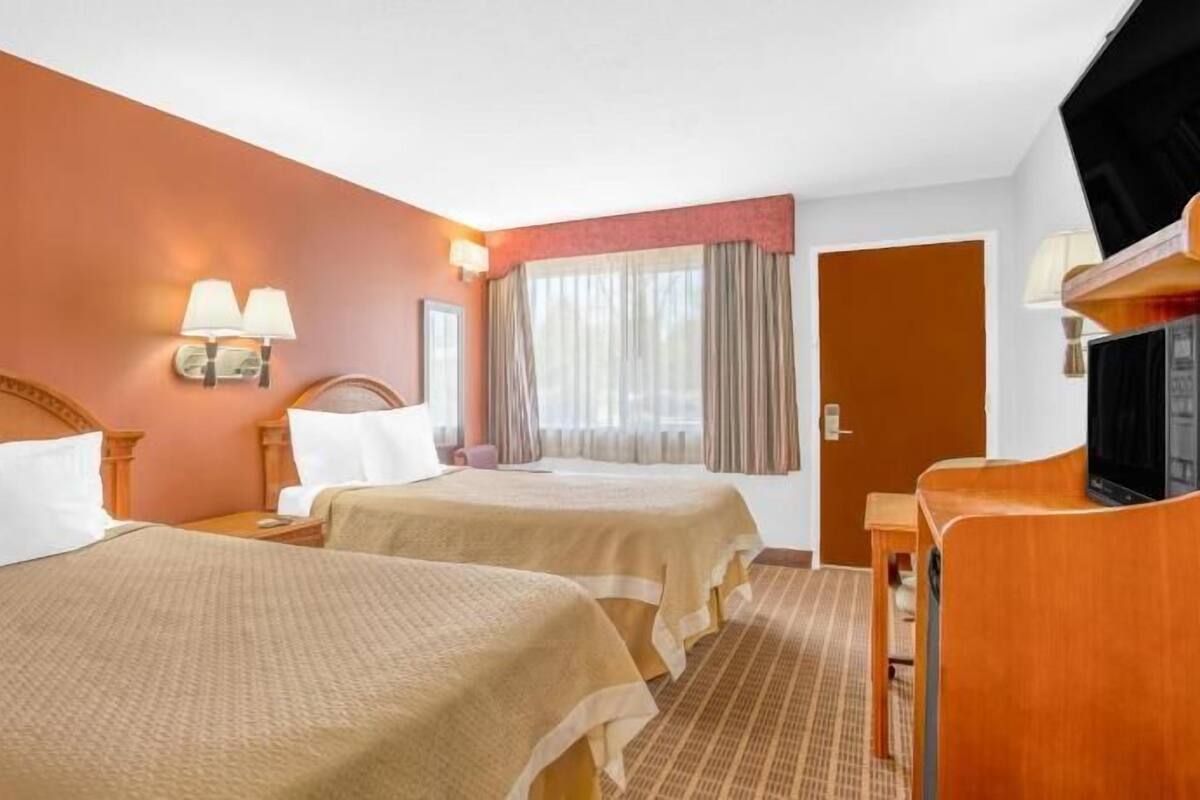 Ein Hotelzimmer mit zwei Betten, einem Fernseher, einem Schreibtisch und einem fensterbepflanzten Fenster.