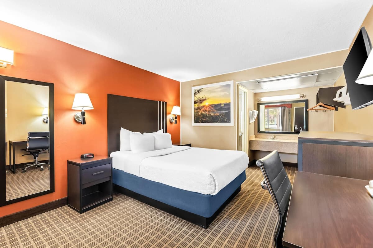 Ein Hotelzimmer mit Bett, Nachttischen, einem Schreibtisch, einem Sessel, einem Spiegel und einem Bild an der Wand.