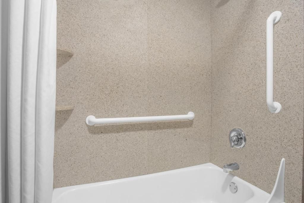 A bathroom with a bathtub, a shower, and a handrail.