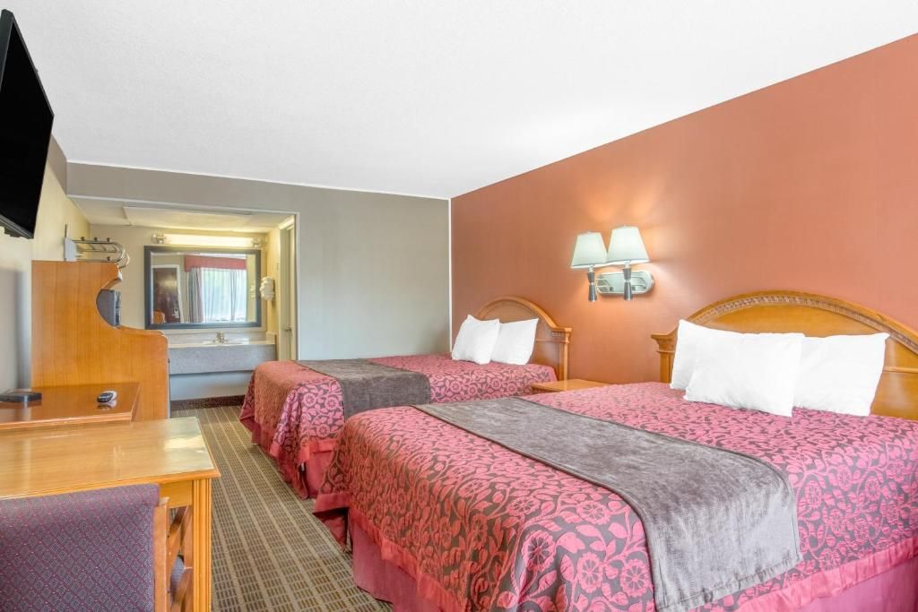 A hotel room with two beds, a desk, a television, and a bathroom visible through an open door.