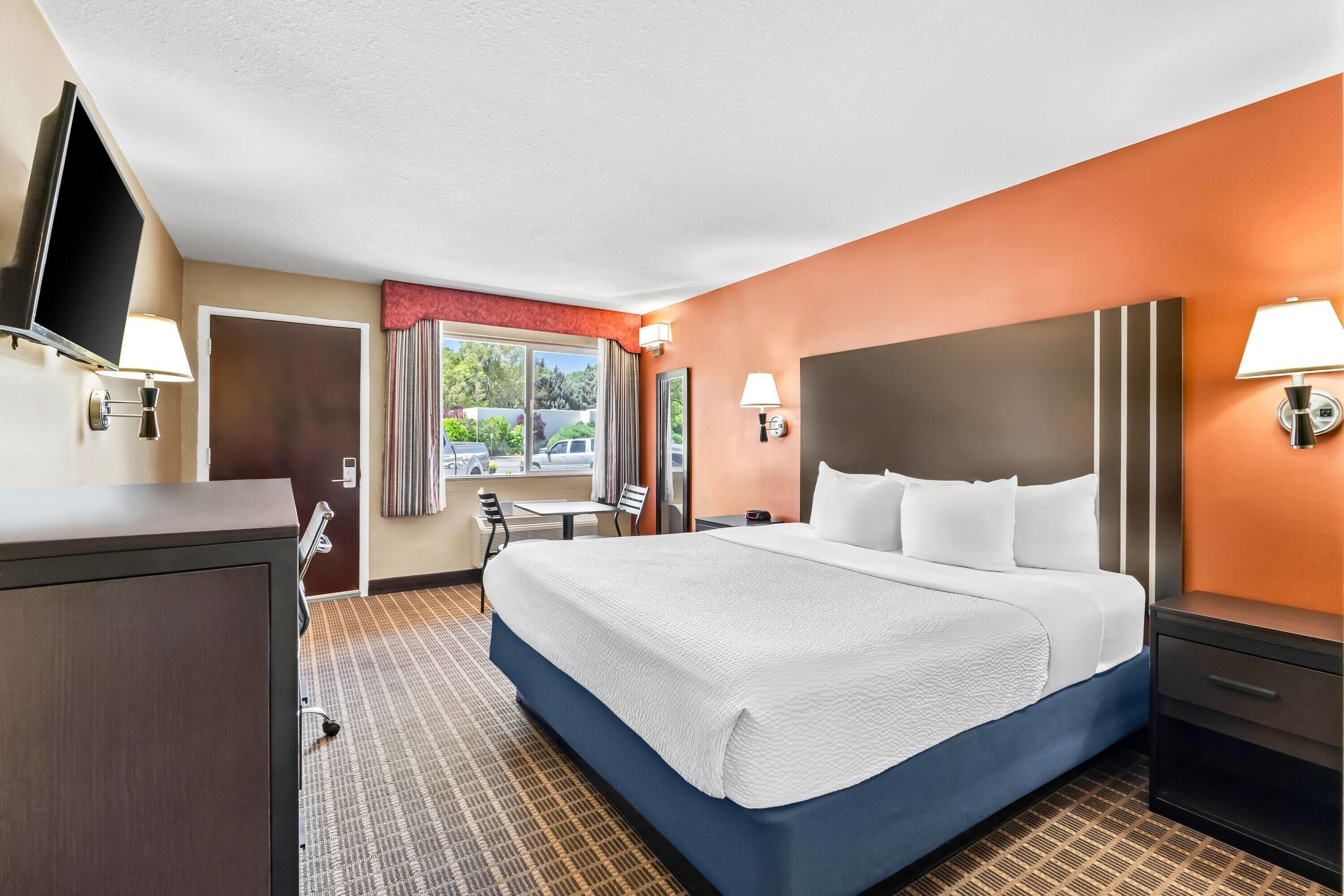 A hotel room with a large bed, a desk, a chair, a TV, and a window with curtains.