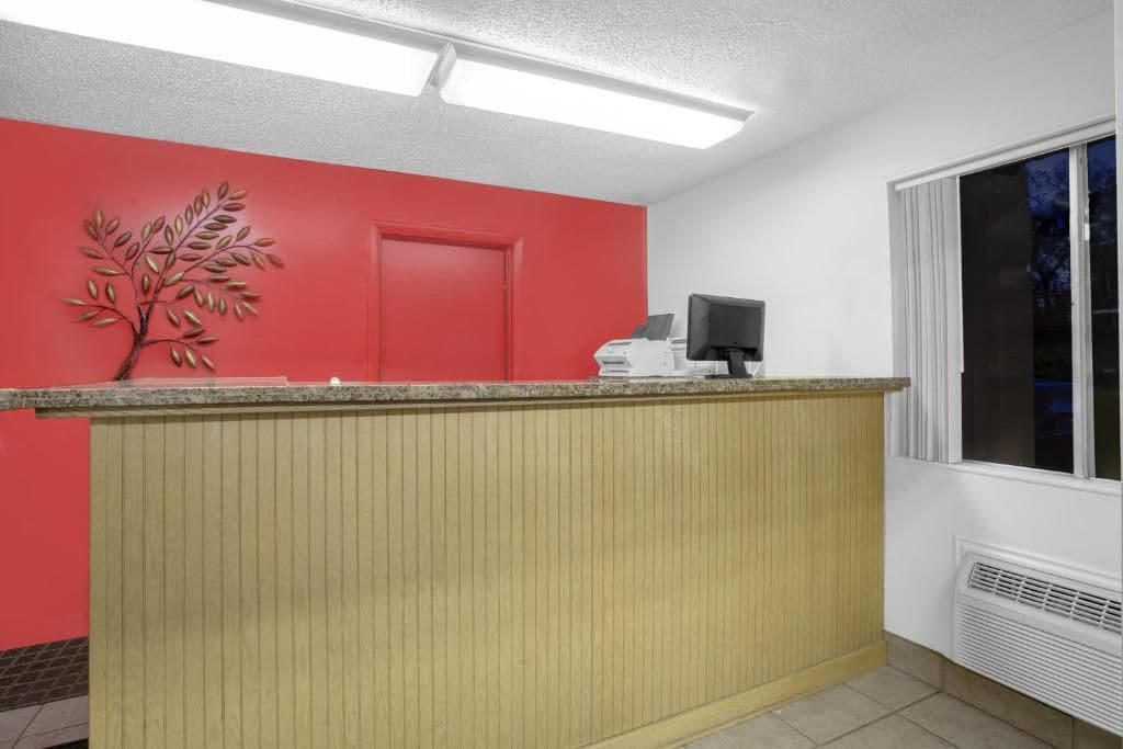 A reception area with a red wall, a wooden panel counter, a door, and a window with blinds.