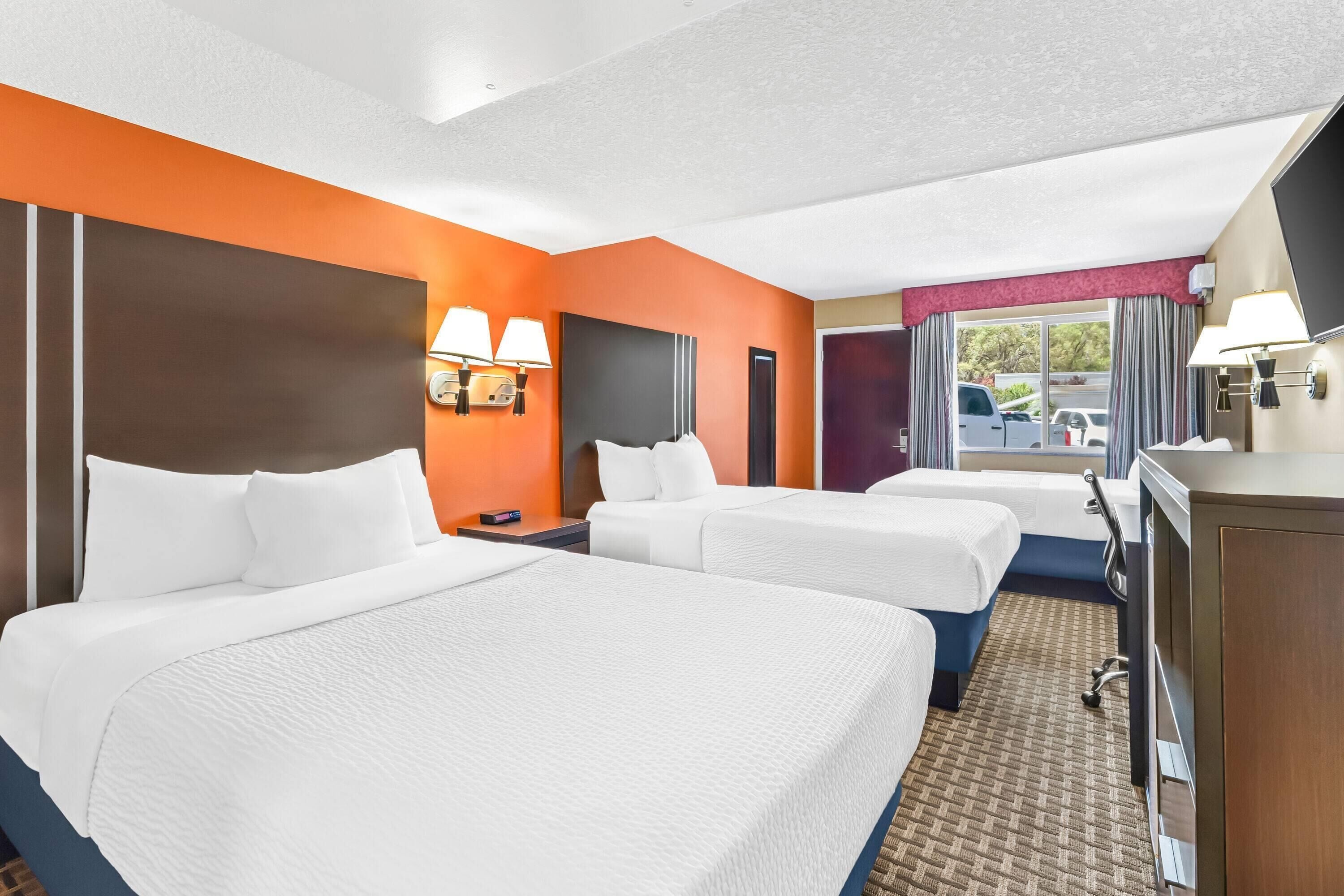A hotel room with two beds, a desk, and a TV.
