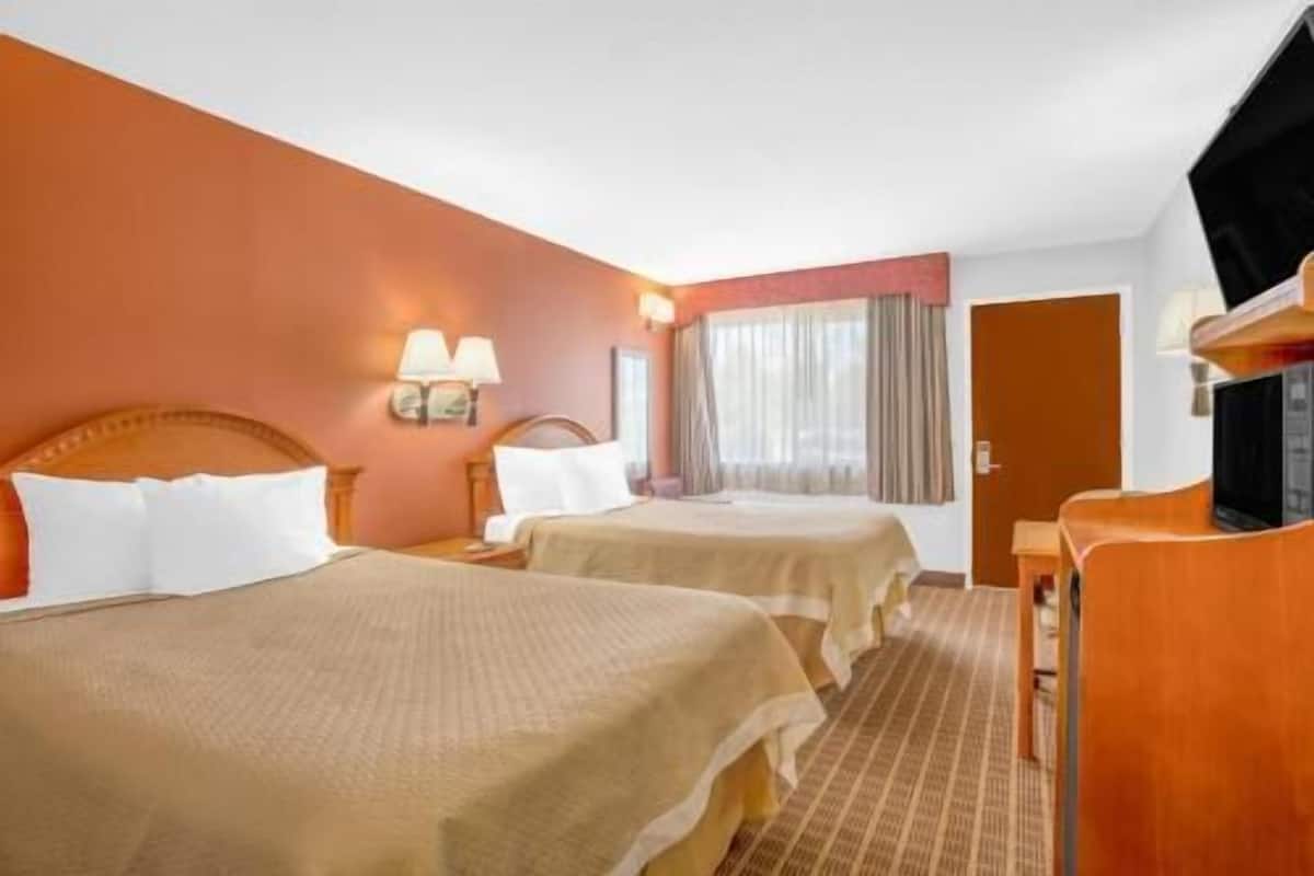 Ein Hotelzimmer mit zwei Betten, einem Fernseher, einem Schreibtisch und einem fensterbepflanzten Fenster.
