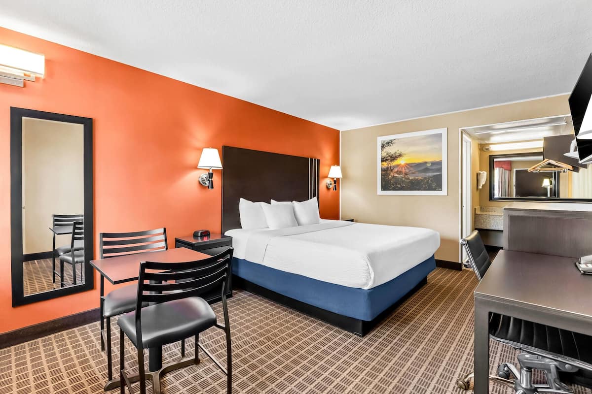 Ein Hotelzimmer mit einem großen Bett, einem Schreibtisch mit Stuhl, einem kleinen Tisch und einem Spiegel.