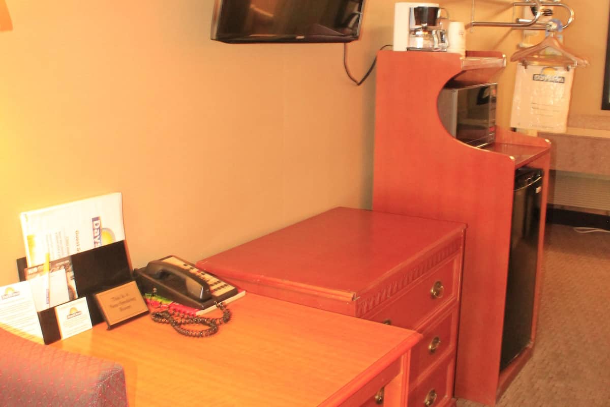 Ein kleines Hotelzimmer mit einem Holztisch, einem Stuhl, einem an der Wand befestigten Fernseher, einer kleinen Küchenzeile mit einer Mikrowelle und einem Mülleimer.