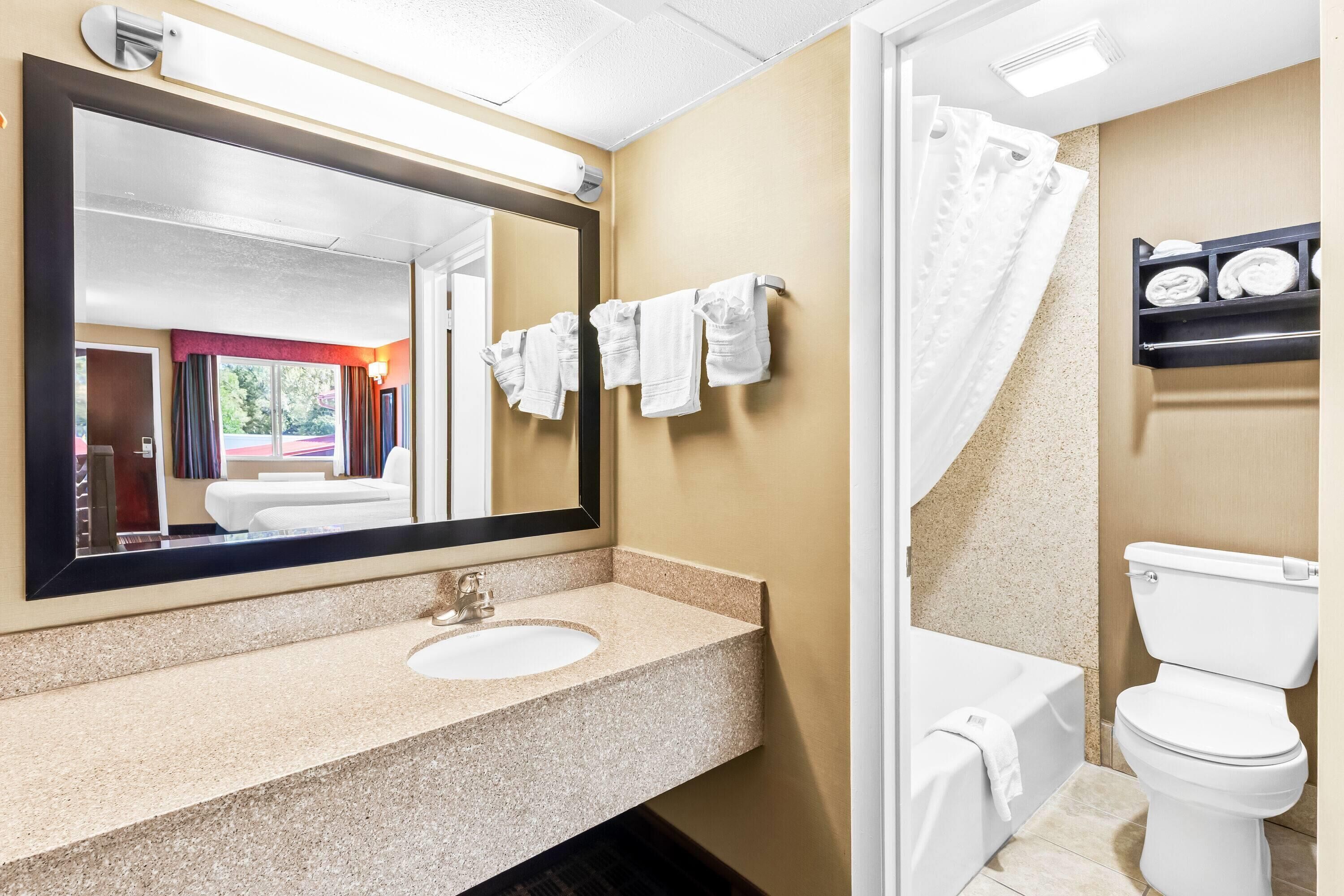 A bathroom with a sink, mirror, white towels, a shower curtain, and a toilet.