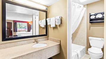 A bathroom with a sink, mirror, white towels, a shower curtain, and a toilet.