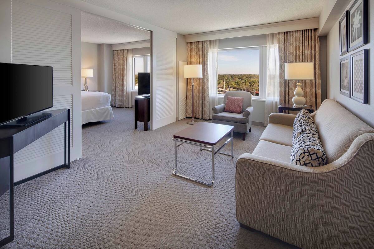 A hotel room with a television, a sofa, a chair, a small table, and a bed.