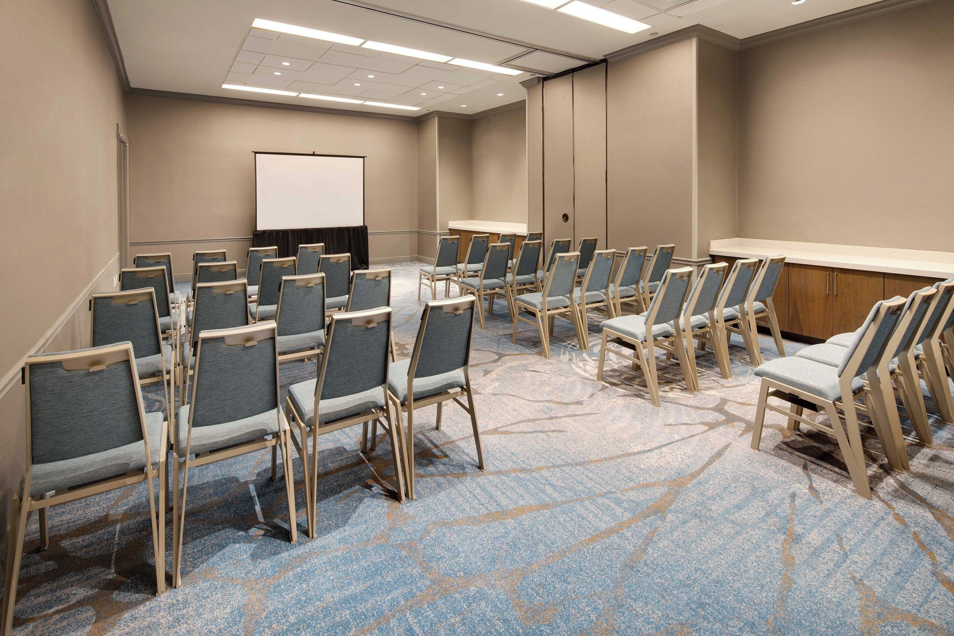 A conference room with rows of chairs, a projector screen, and a carpeted floor.