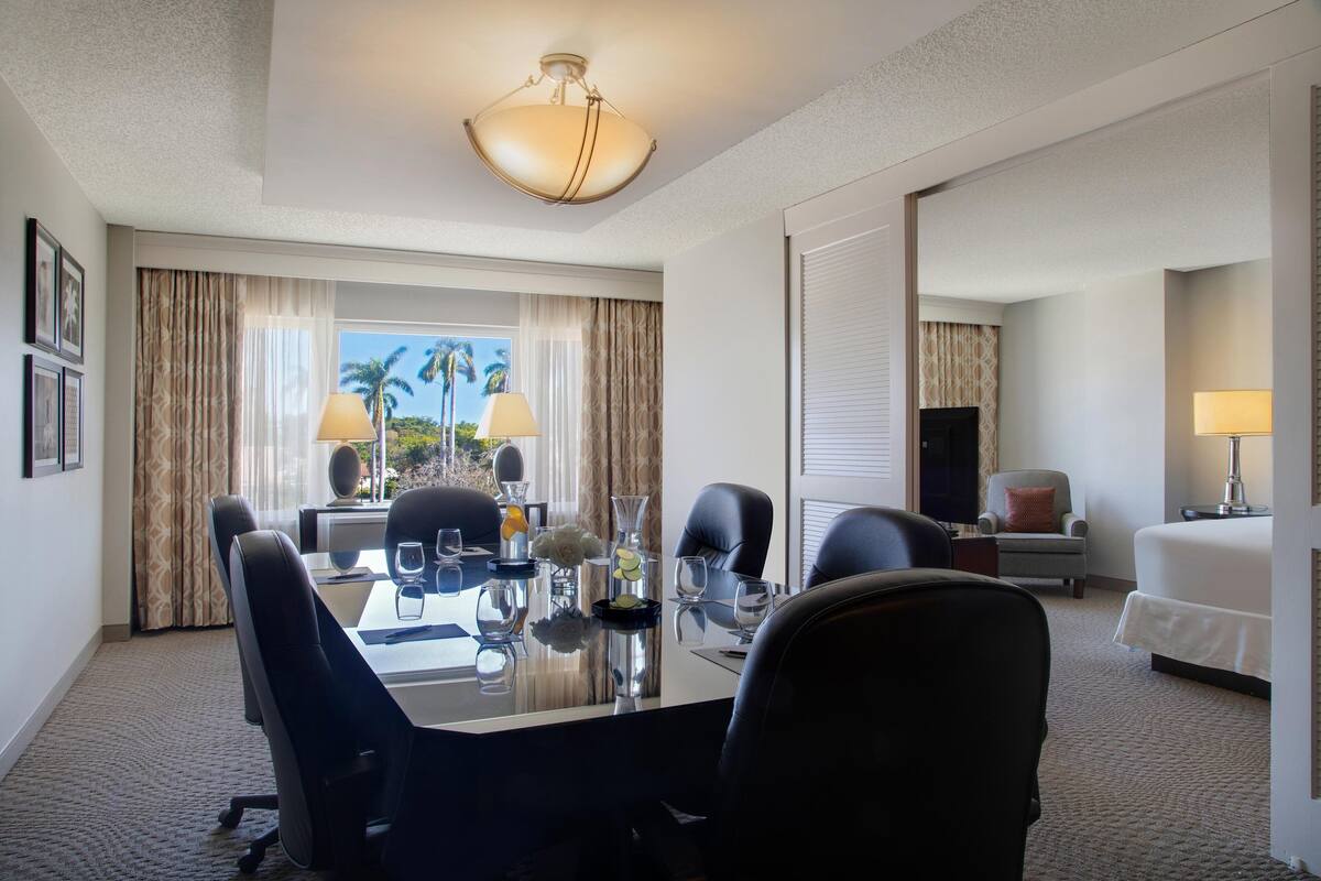 A hotel room with a dining area, a bed, a TV, and a window with curtains.