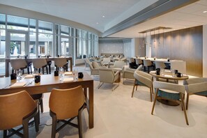 Un comedor amplio con varias mesas y sillas, ventanas grandes que aportan luz natural, y un diseño de interiores moderno.