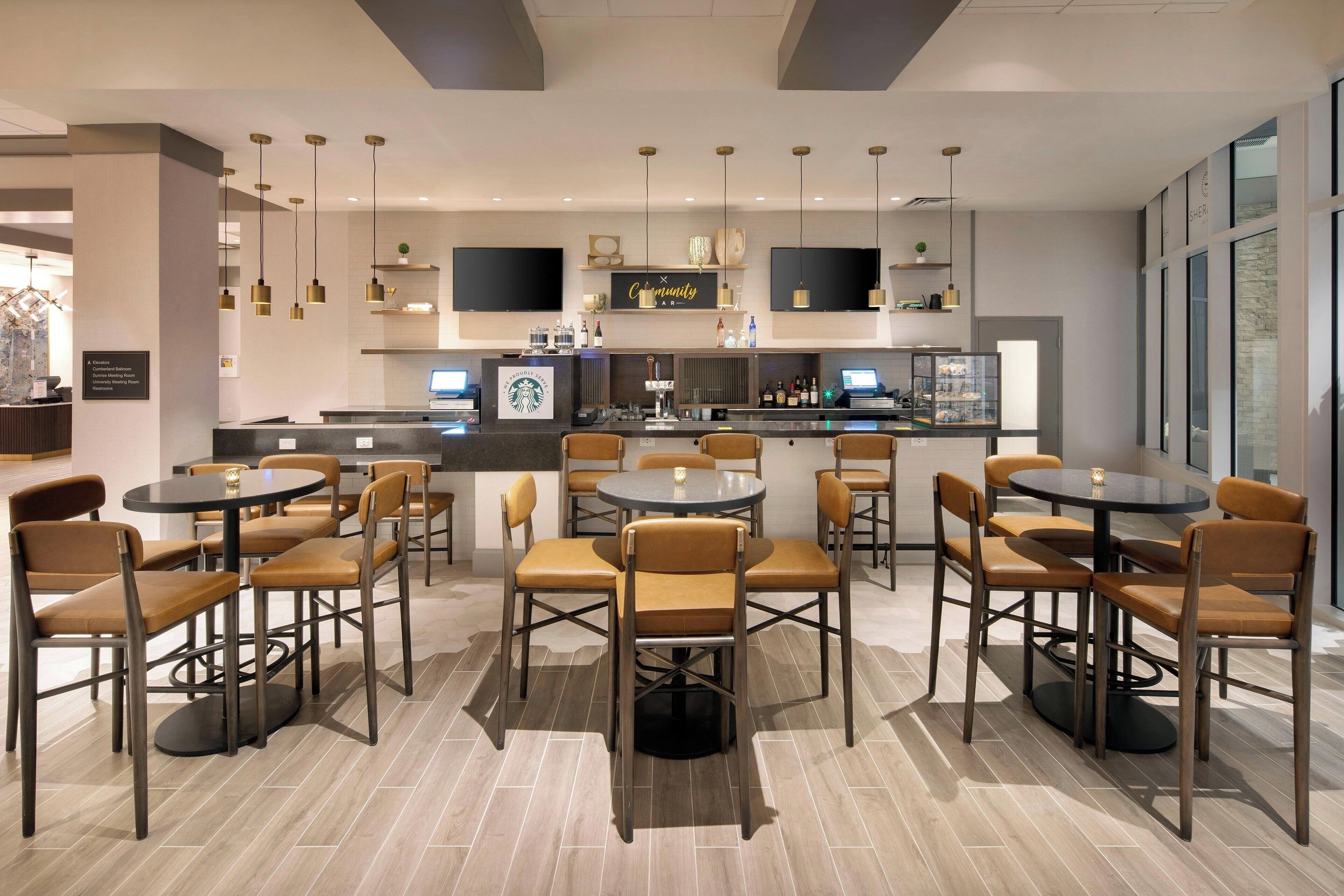 Una moderna hall d'albergo con diverse aree salotto, un bancone Starbucks e un'area bar.