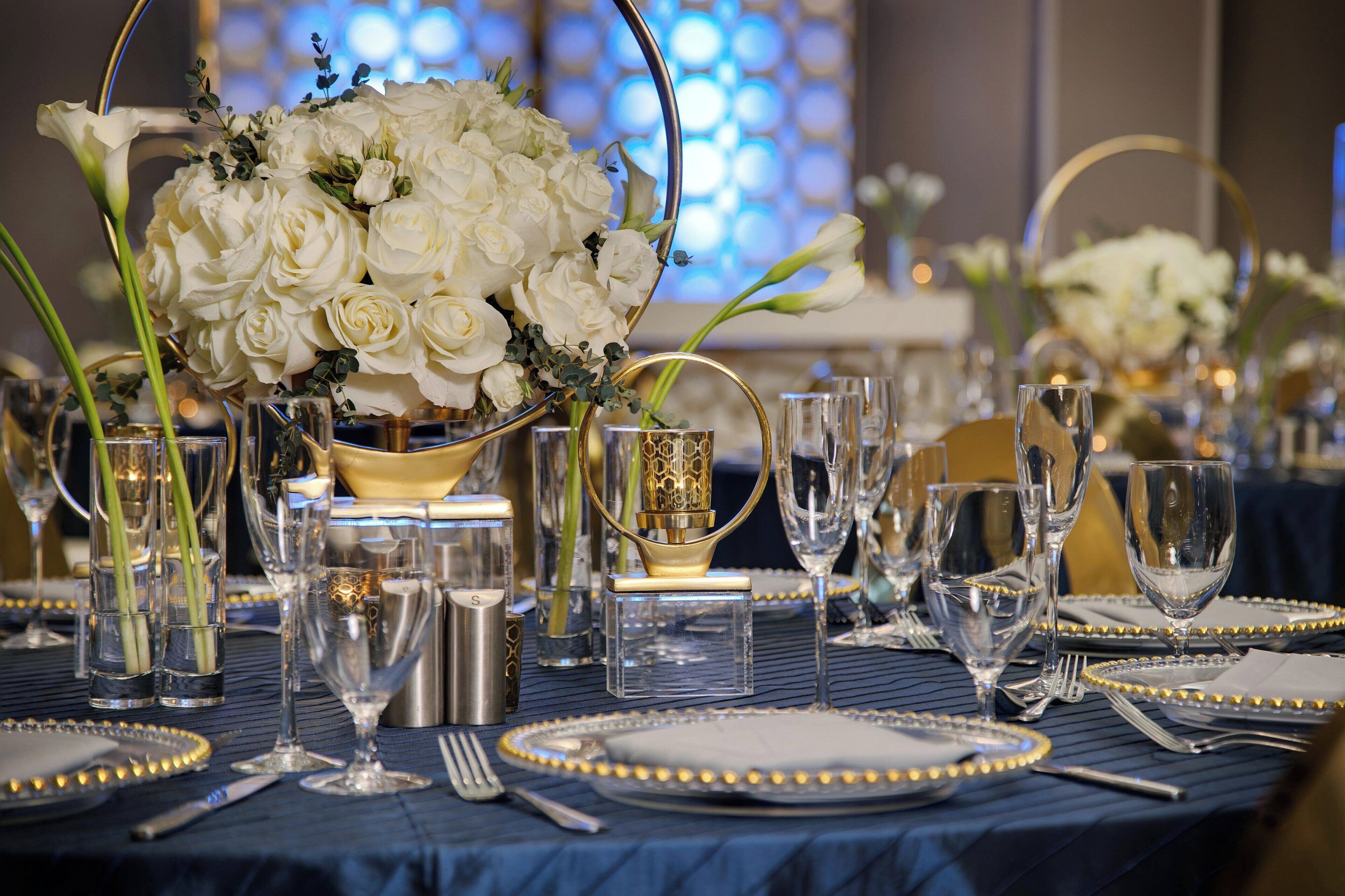 A table set for a formal event with white flowers, clear glassware, and gold accents.