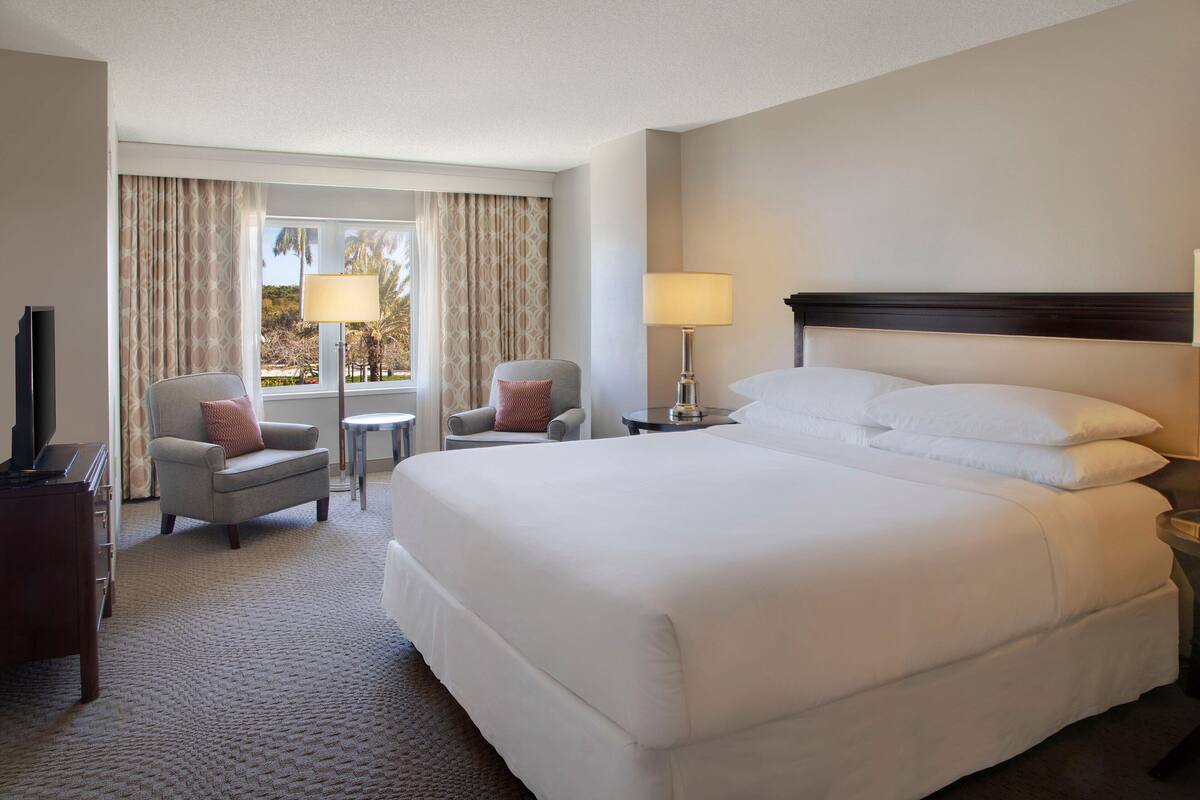 A hotel room with a large bed, two armchairs, a small table, and a TV.