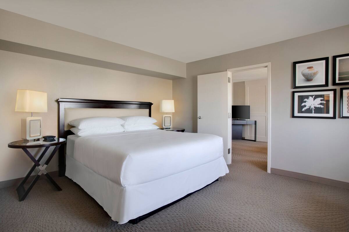 A hotel room with a large bed, two bedside tables with lamps, a flat-screen TV, and framed artwork on the wall.