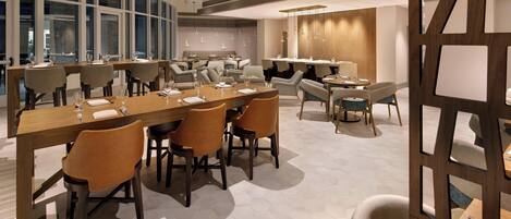 A modern dining area with hexagonal tile flooring, multiple dining tables with chairs, and large windows providing natural light.
