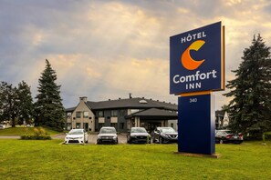 A hotel sign with a modern building in the background. - Comfort Inn Aéroport (Dorval)