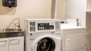 A front-loading washing machine with a digital display, a stainless steel sink, and a white wall.