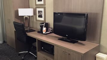 A hotel room with a wooden desk, a flat-screen TV, a coffee maker, a lamp, and a microwave.