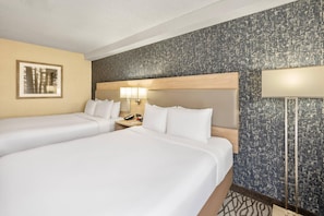 Een hotelkamer met twee bedden, een nachtkastje, een lamp en een lijst met een afbeelding aan de muur.
