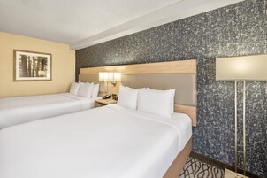 A hotel room with two beds, a nightstand, a lamp, and a framed picture on the wall.