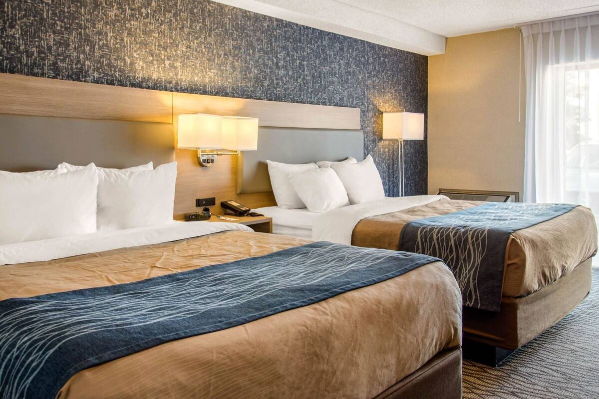 Habitación de hotel con dos camas, cabeceros, lámparas de noche, mesitas de noche y una ventana con cortinas.