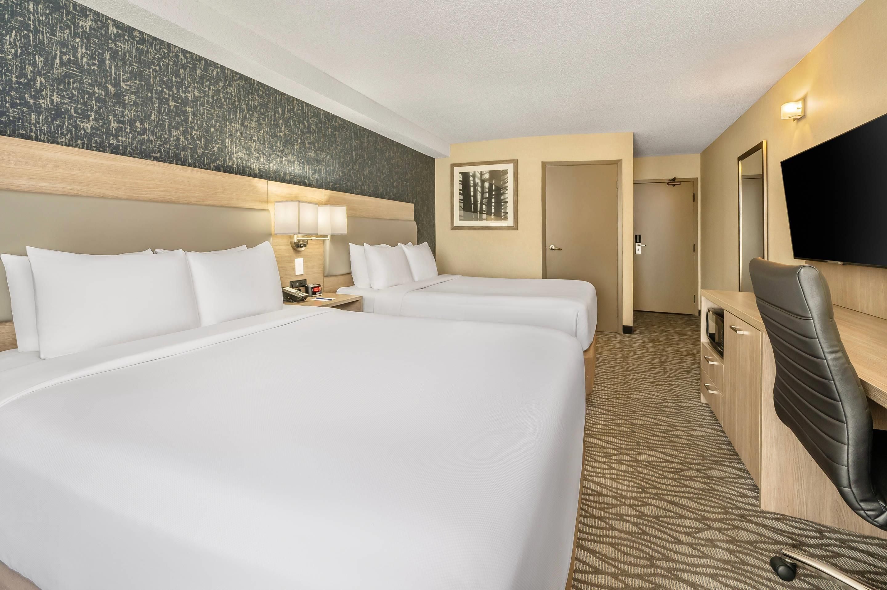 Une chambre d’hôtel avec deux lits, une télévision, un bureau et une porte de salle de bain.