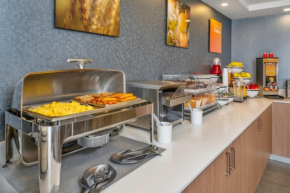 A buffet setup with various food items, a beverage dispenser, and a coffee machine. - Comfort Inn Aéroport (Dorval)