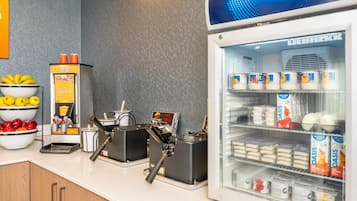 A self-service beverage station with coffee machines and a refrigerator stocked with milk and juice cartons.