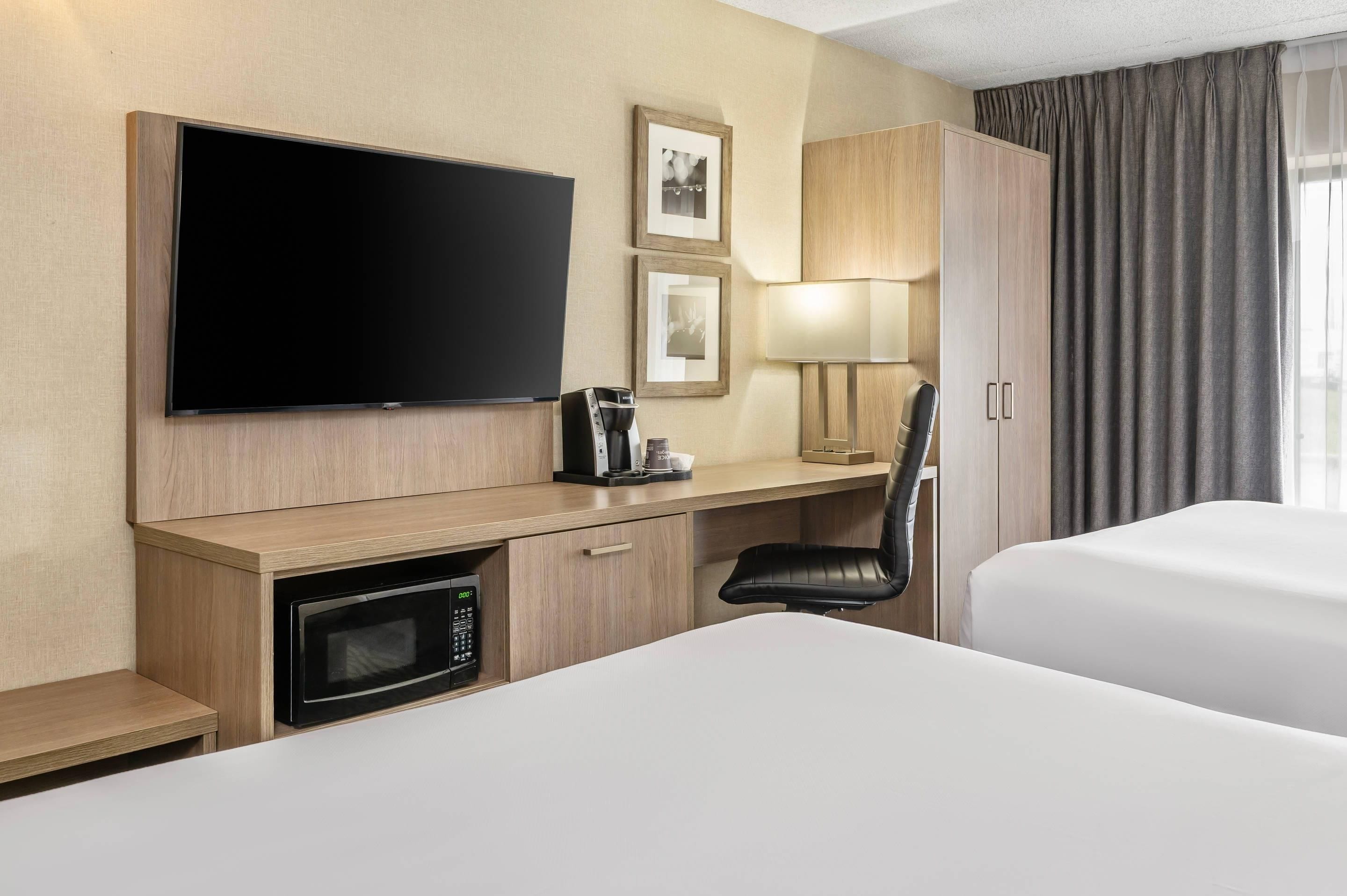 A hotel room with a flat-screen TV, a coffee maker, a microwave, a desk, a chair, and a bed.