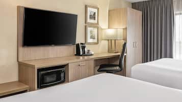 A hotel room with a flat-screen TV, a coffee maker, a microwave, a desk, a chair, and a bed.