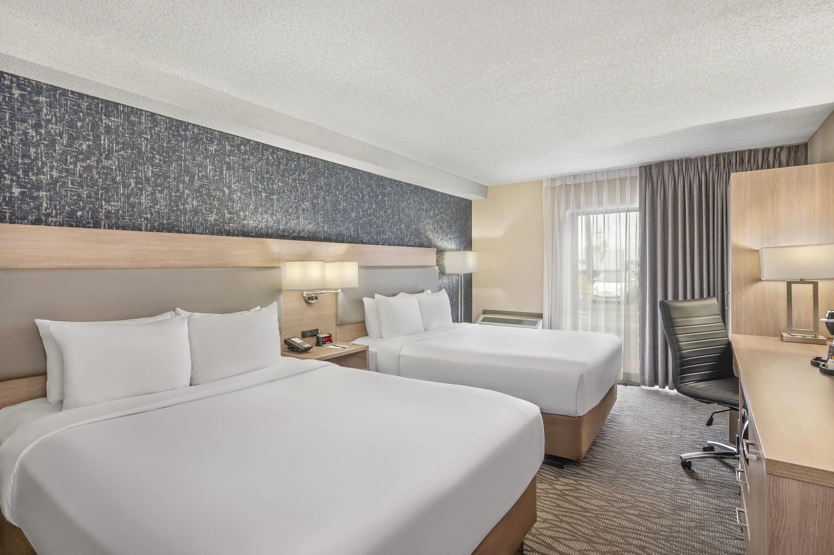 A hotel room with two beds, a desk, a chair, and a large window with curtains.