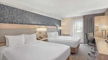 A hotel room with two beds, a desk, a chair, and a large window with curtains.