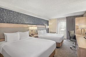 A hotel room with two beds, a desk, a chair, and a large window with curtains. - Comfort Inn Aéroport (Dorval)