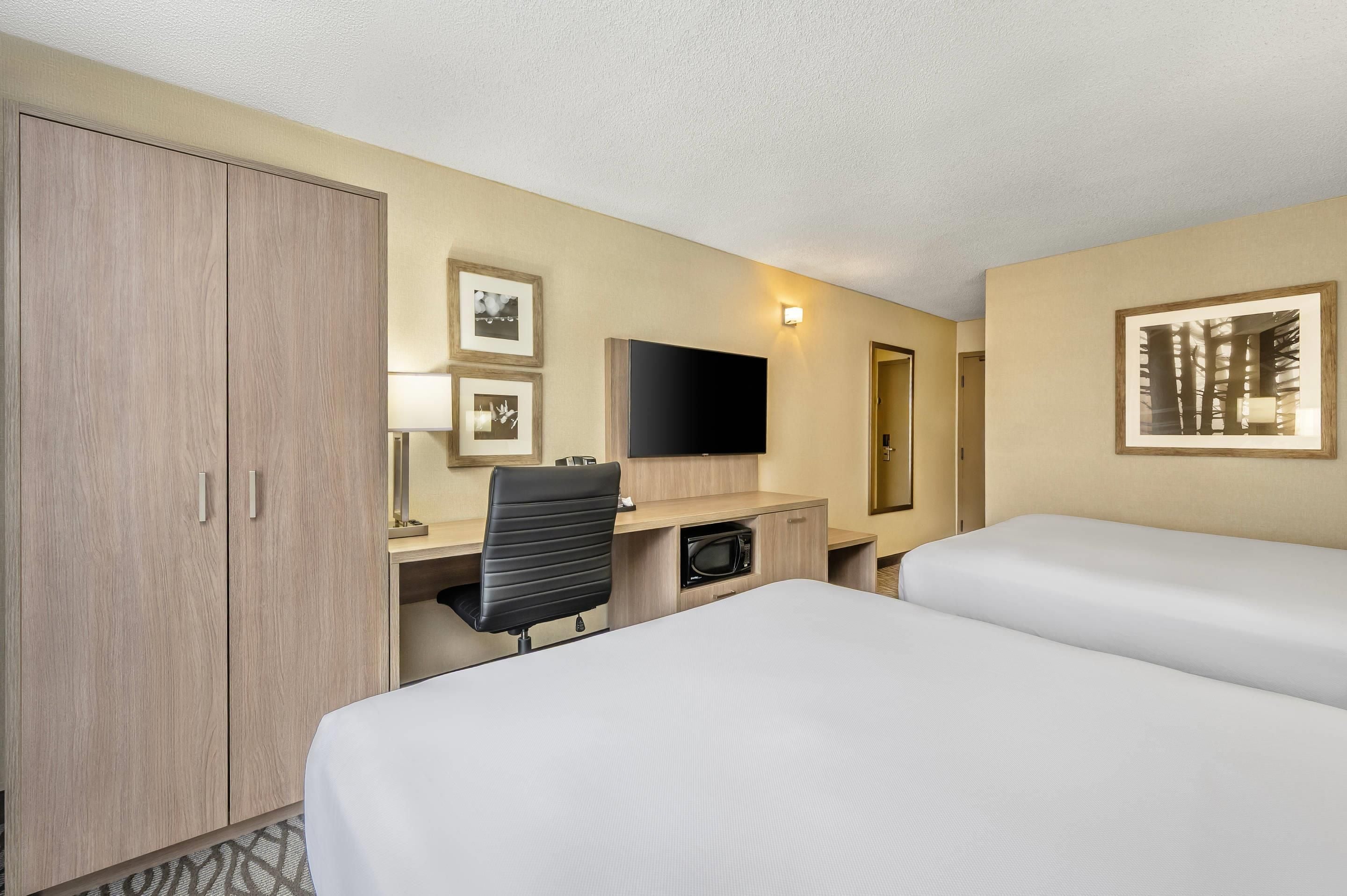 Habitación de hotel con escritorio, dos camas, armario, televisión de pantalla plana y cuadros en las paredes.