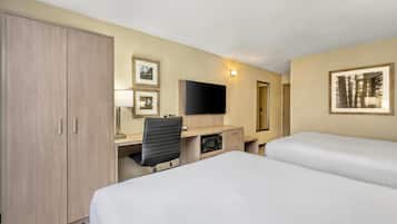 Habitación de hotel con escritorio, dos camas, armario, televisión de pantalla plana y cuadros en las paredes.